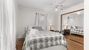 Een slaapkamer met een bed, een nachtkastje met een lamp, een plafondventilator en een grote spiegel.