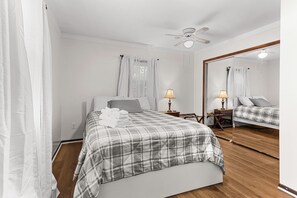Une chambre à coucher avec un lit, une table de chevet avec une lampe, un ventilateur de plafond et un grand miroir.