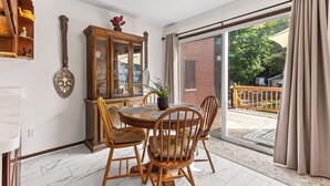 Een eethoek met een houten tafel en stoelen, een kast met glazen deuren, en uitzicht door een grote schuifpui op een terras.