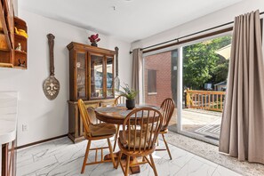 Un coin repas avec une table et des chaises en bois, un meuble avec des portes en verre, et une vue sur une terrasse extérieure, accessible par une grande porte-fenêtre coulissante.