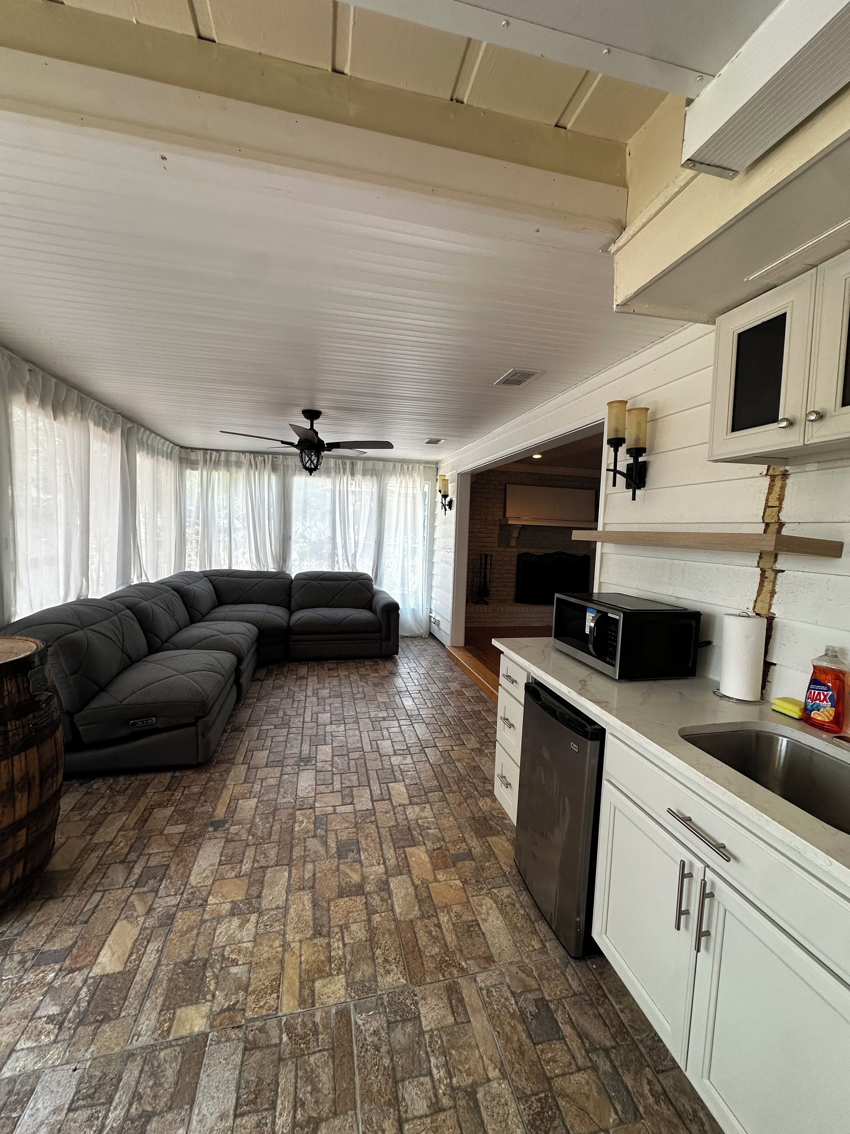 A modern kitchen with a sectional sofa, a ceiling fan, and a stone-patterned floor.