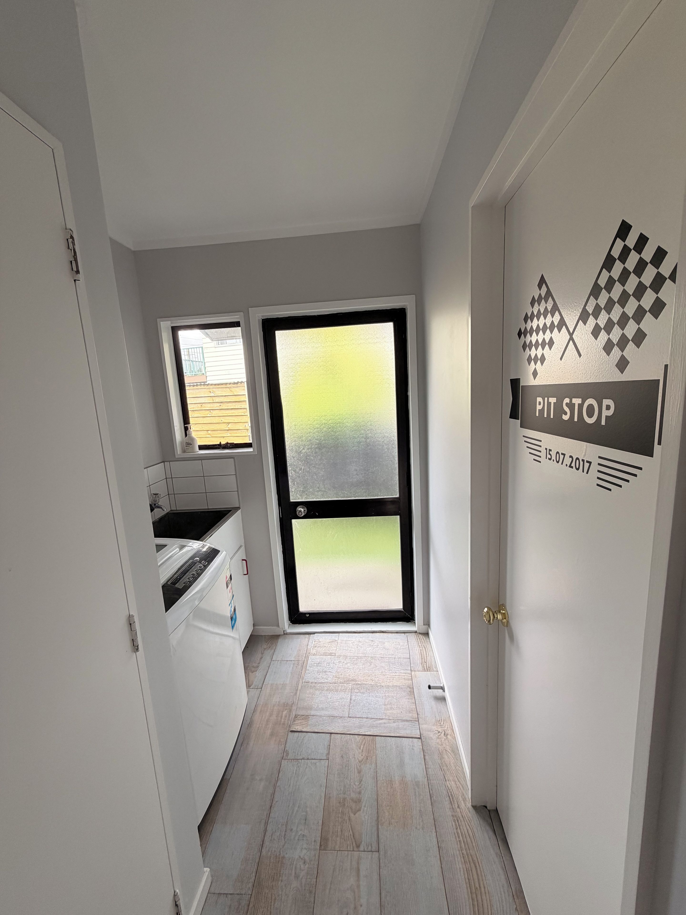 A narrow hallway with a kitchen area on the left, a large frosted glass door, and a door with 'PIT STOP' signage.