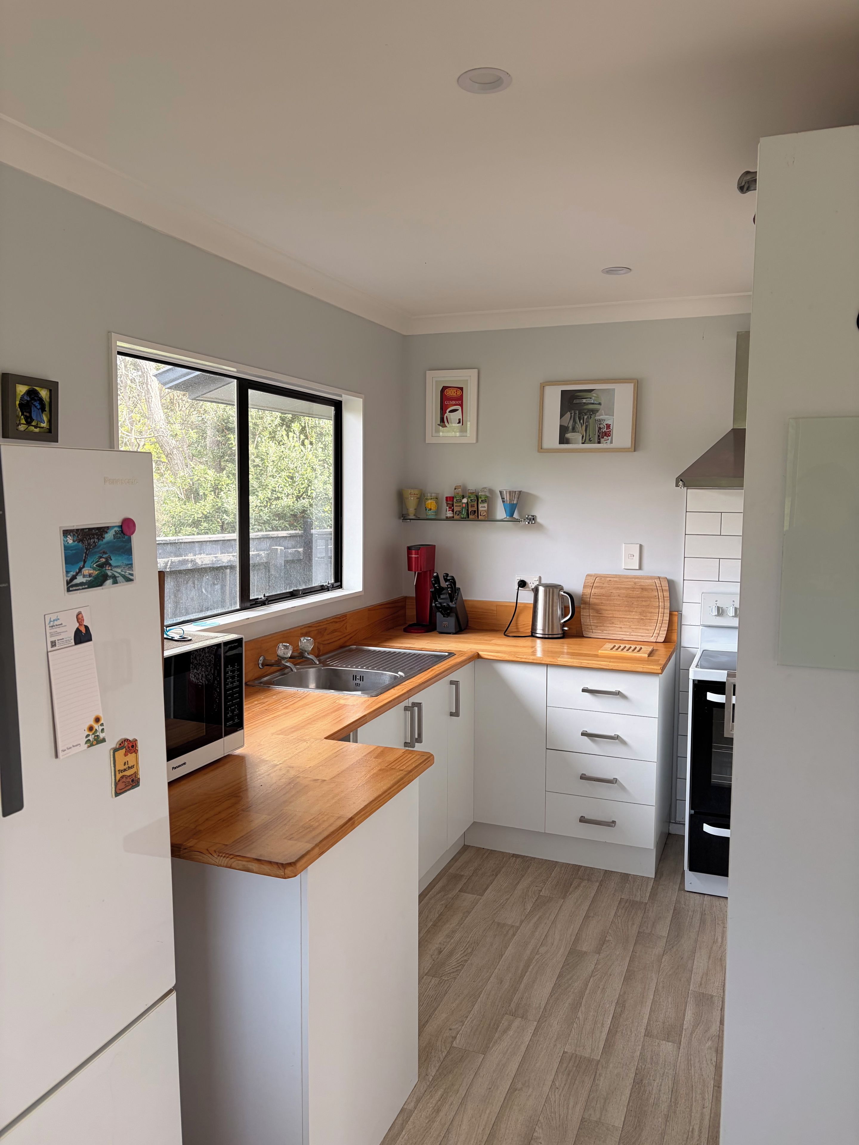 A compact kitchen with white cabinets, a wooden countertop, a built-in microwave, and a window providing natural light.