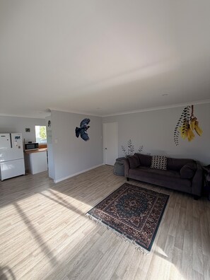 A spacious living area with a sofa, a patterned rug, and wall art. - Kiwiana themed bach, perfect for family getaways or a retreat near the beach! (Waikanae Beach)