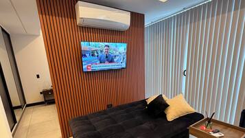 Un saló modern amb un sofà fosc, una paret d'accent de fusta, un televisor penjat i una taula auxiliar de fusta petita.