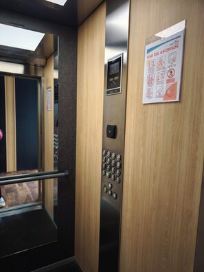 An elevator interior with a digital display, control panel, and safety instructions.