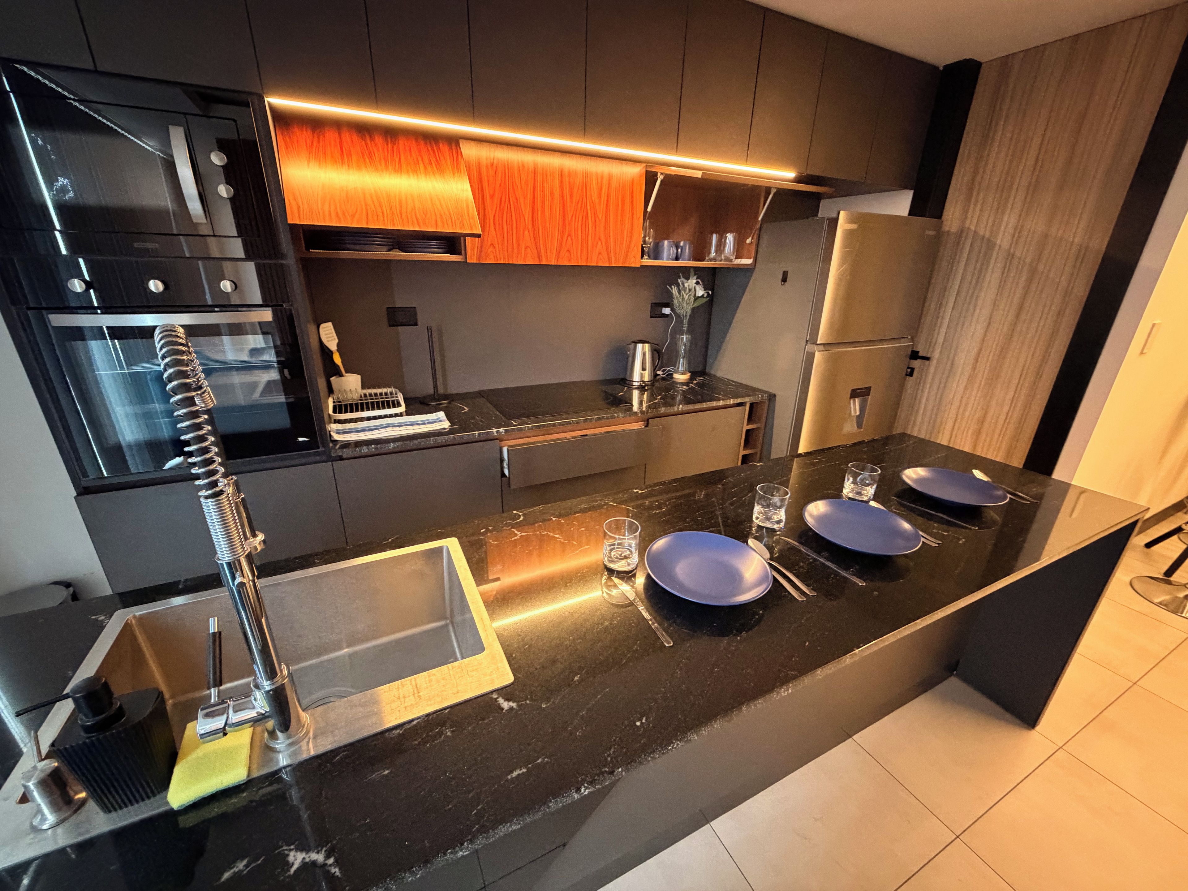 Une cuisine moderne avec un plan de travail noir, des appareils en acier inoxydable et un pare-feu en bois.