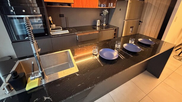 Una cocina moderna con encimera negra, electrodomésticos de acero inoxidable y salpicadero de madera.