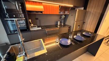 Une cuisine moderne avec un plan de travail noir, des appareils en acier inoxydable et un pare-feu en bois.
