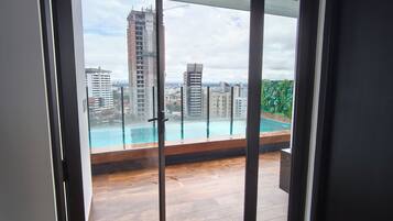 A modern interior with a large glass door leading to an outdoor balcony with a view of a swimming pool and surrounding buildings.