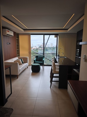 A modern living space with a sofa, ottoman, and dining area, featuring a city view through large windows.