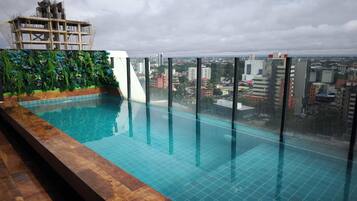Une piscine à débordement située sur le toit, offrant une vue sur la ville, entourée d’une terrasse en bois et d’un mur végétal.