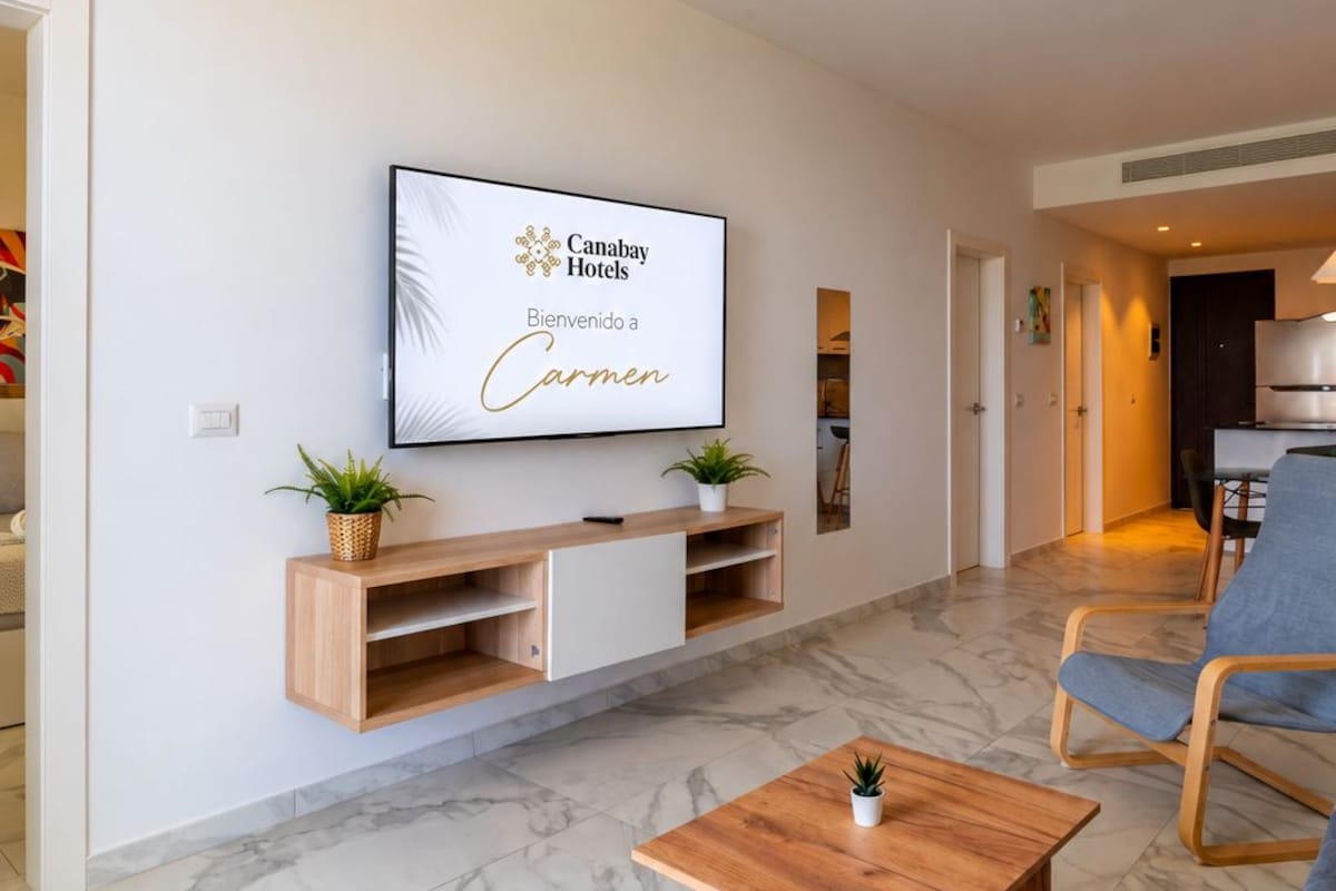 Una sala de estar moderna con un televisor de pantalla plana, estanterías de madera, una mesa de centro y un sillón azul.