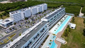 Un hotel de varios pisos con piscina en la azotea y zona ajardinada alrededor de la piscina.