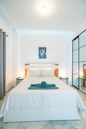 Habitación de hotel con una cama grande, cabecera, dos mesitas de noche, una obra de arte colgada en la pared y un ventanal amplio.