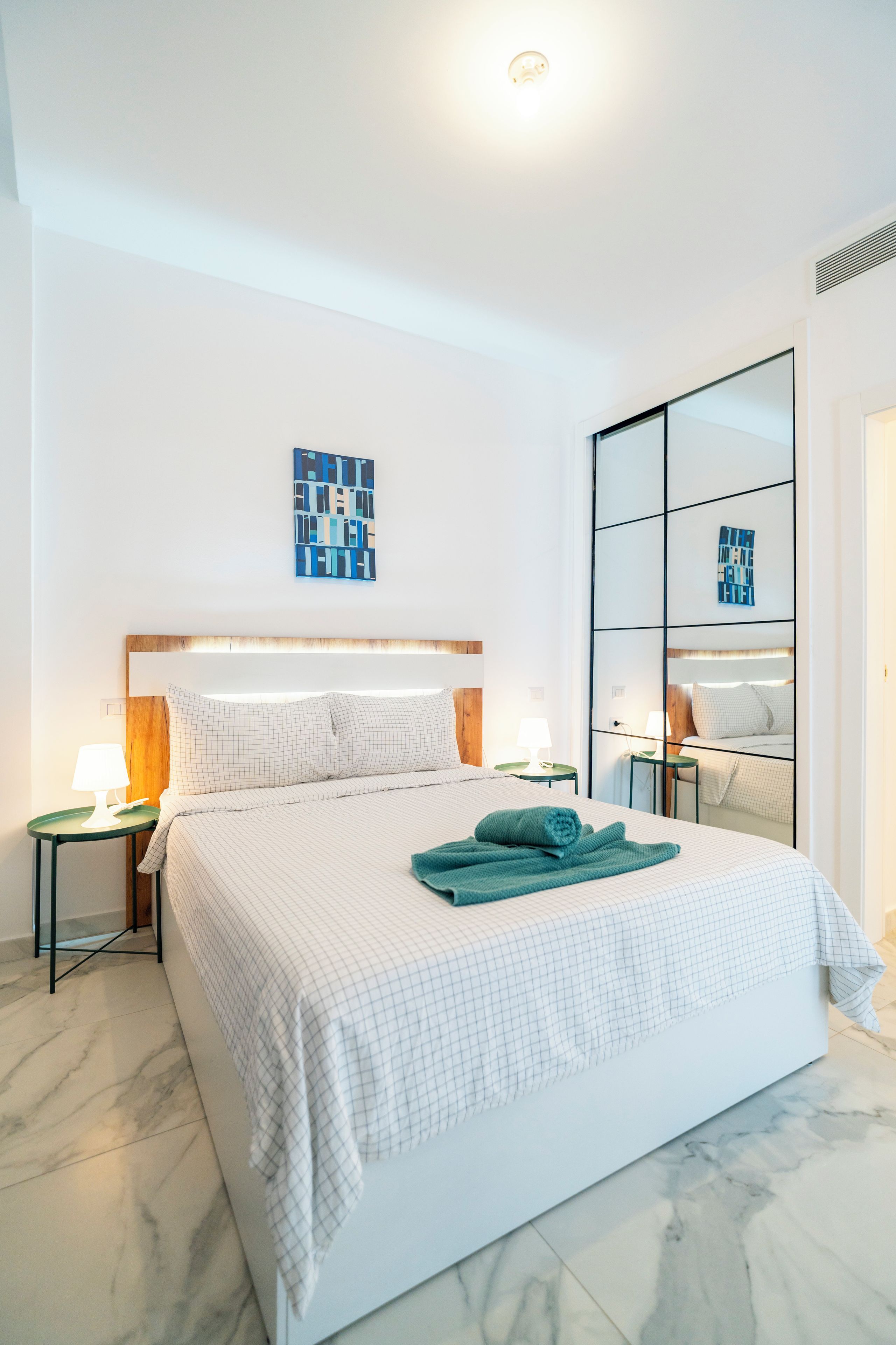 Une chambre d’hôtel avec un grand lit, une table de chevet avec une lampe, une œuvre d’art accrochée au mur et un miroir.