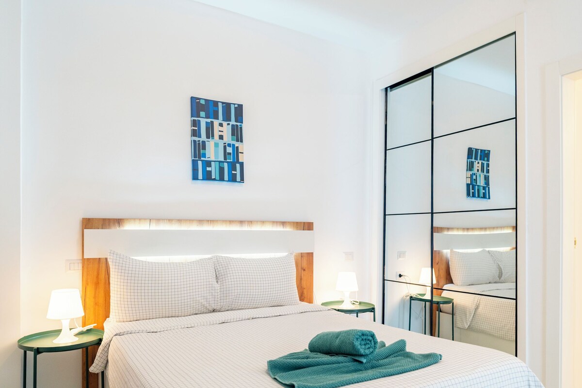 Una habitación de hotel con una cama grande, una mesita de noche con lámpara, una obra de arte en la pared y un espejo.