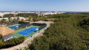 A tennis court complex with multiple courts, surrounded by dense greenery and a view of a coastal town. - Cana Rock  (Punta Cana)