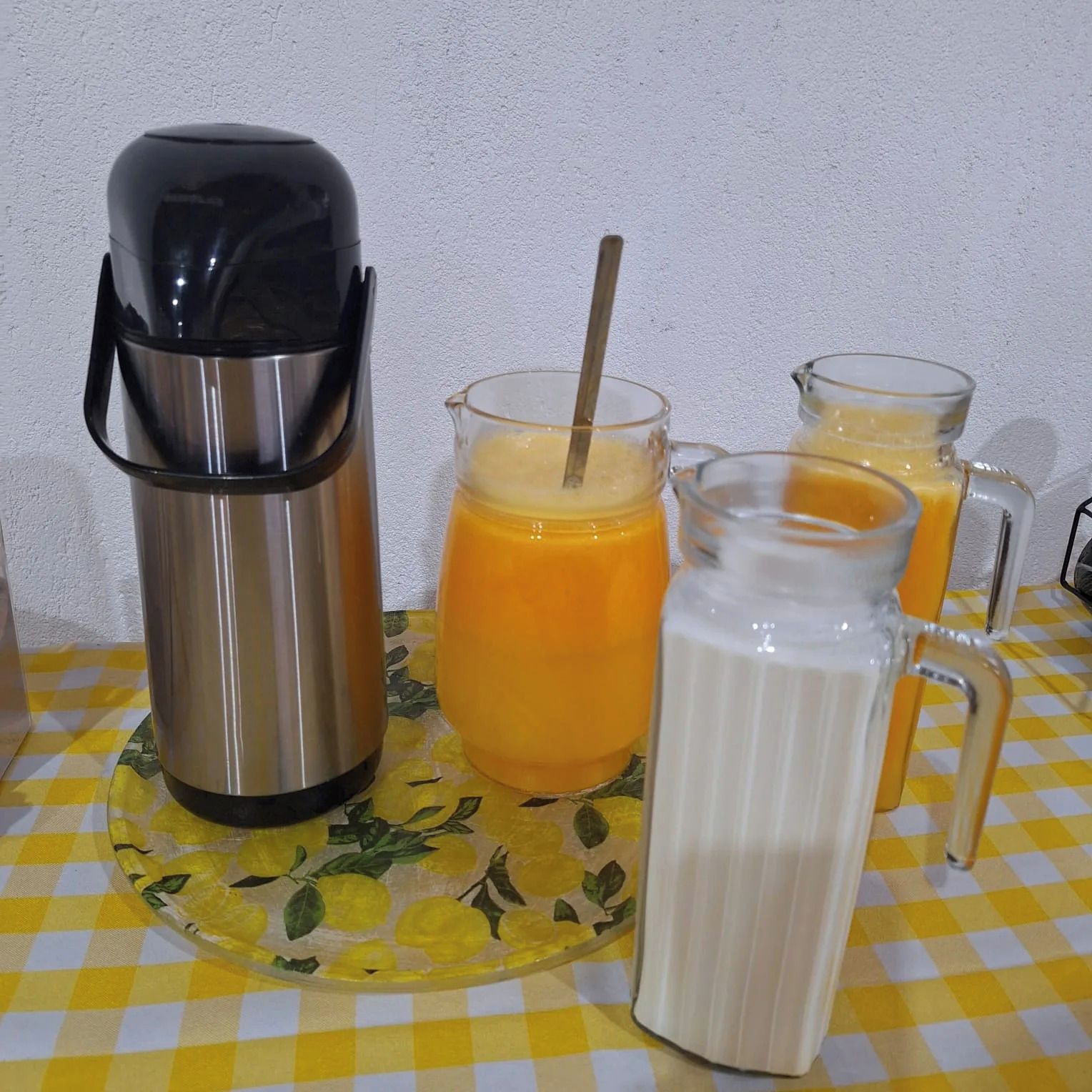 A stainless steel thermos, two glass mugs with straws, and a glass pitcher on a checkered tablecloth.
