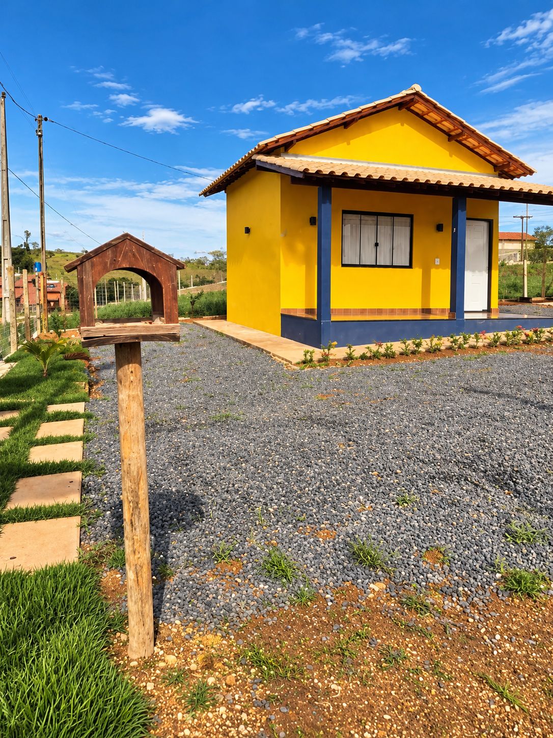 A yellow building with a red roof, a wooden structure in front, and a gravel driveway.