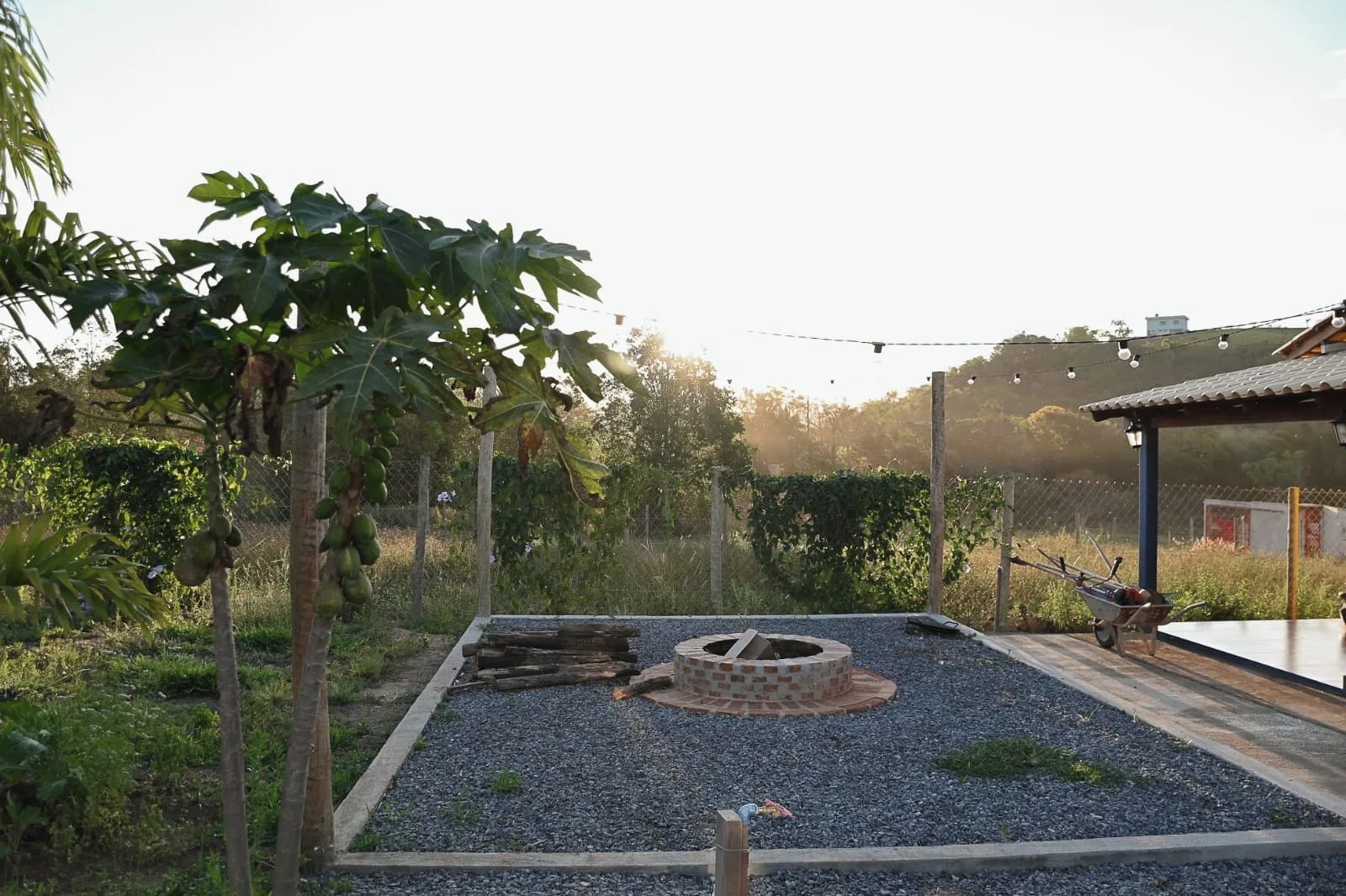 Un jardín con una estructura circular de ladrillo, senderos de grava y una valla de madera.