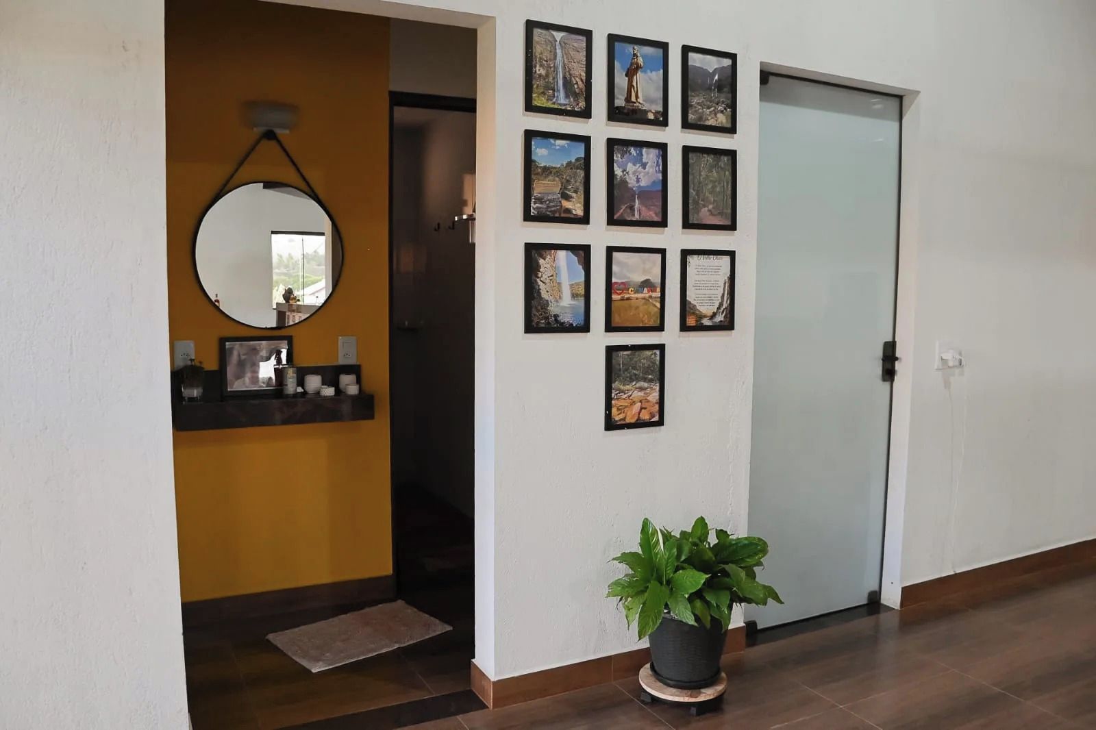 A hallway with a mirror, a potted plant, and a wall adorned with framed pictures.