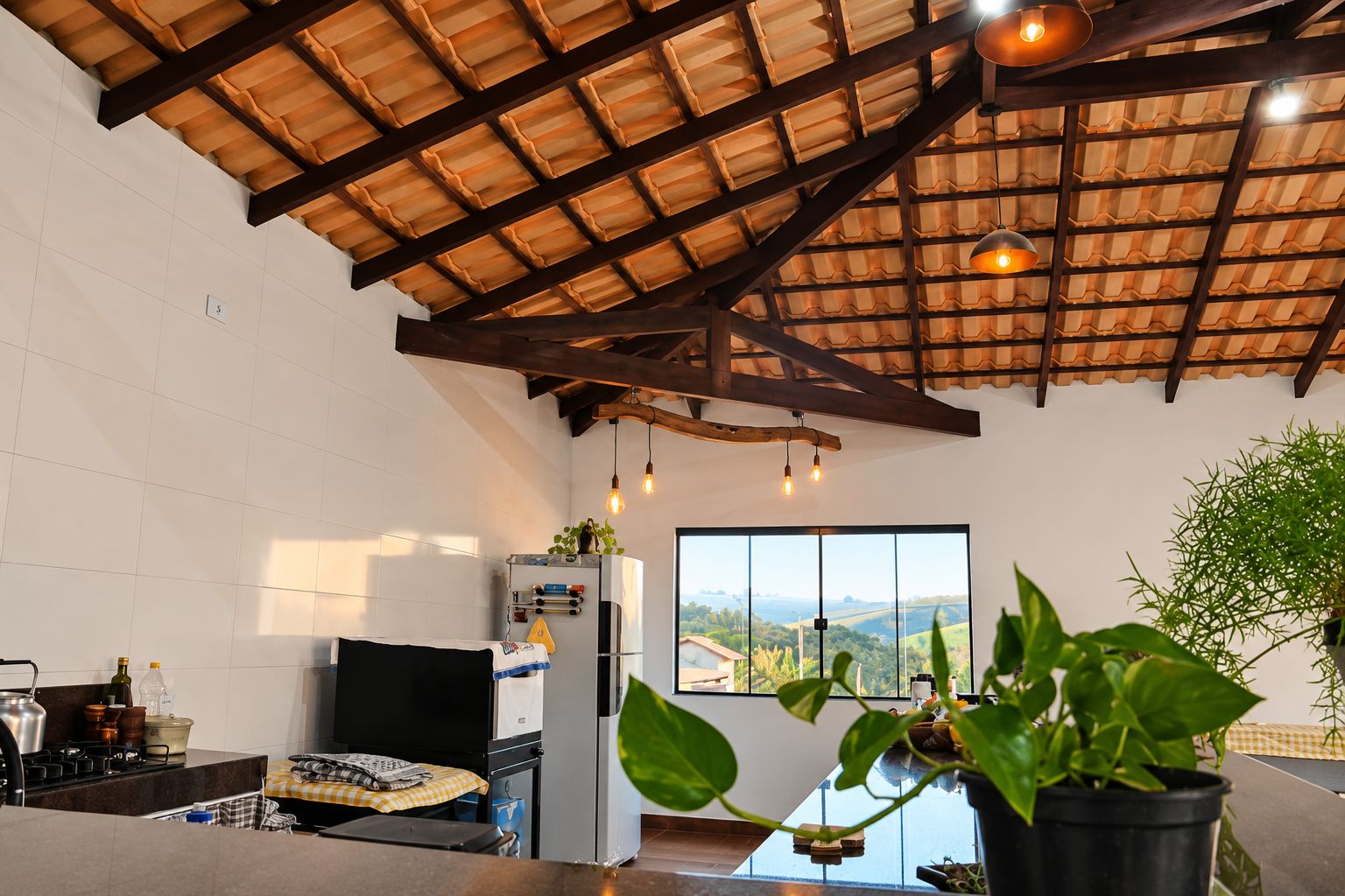 A kitchen with a large window, a ceiling with exposed beams, and a view of the countryside.