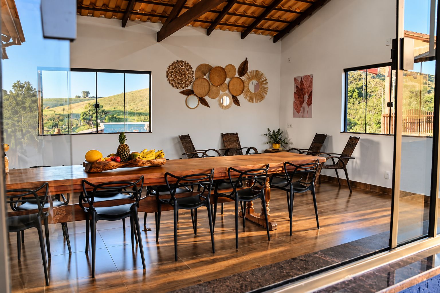 A dining area with a wooden table, black chairs, and a view of a landscape through large windows.