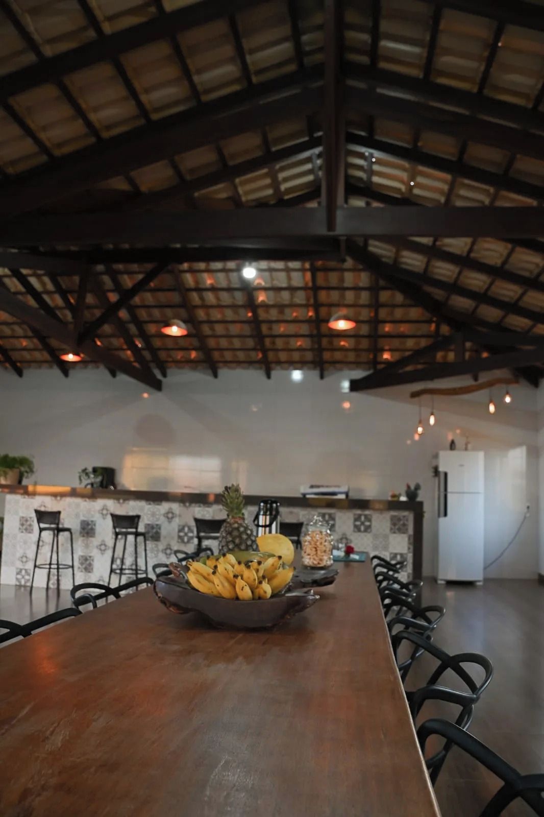 A spacious dining area with a long wooden table, black chairs, and a kitchen in the background.