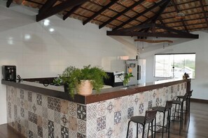 A modern kitchen with a tiled backsplash, a central island with a plant, bar stools, and a view of the outside through large windows. - Chalés do Popô na Canastra (São Roque de Minas)