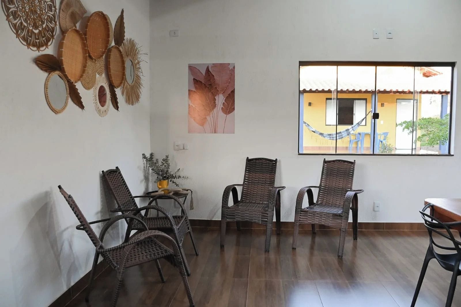 A room with wicker chairs, a small table with a vase, and a window with a view of buildings.
