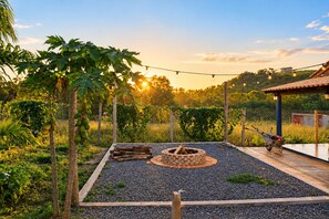 Un jardín con un pozo de fuego, una carretilla y luces colgantes.