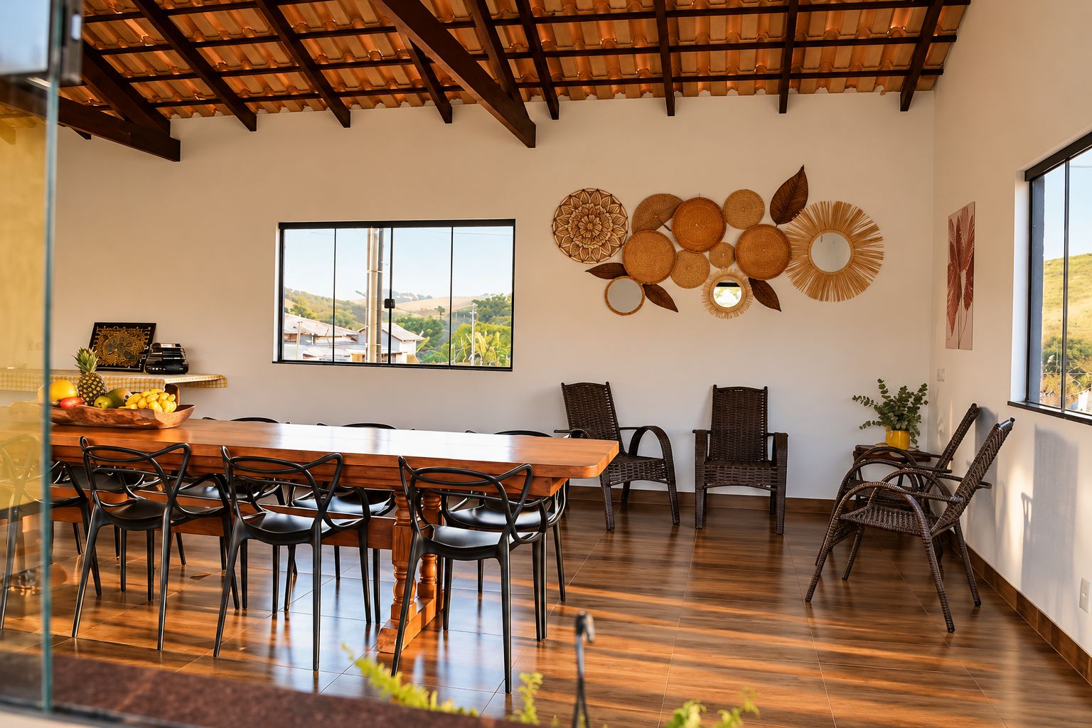 Uma sala de jantar com uma mesa de madeira comprida, cadeiras pretas e vista para o exterior através de grandes janelas.