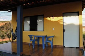 A room with a yellow wall, a door, a window, and a table with chairs. - Chalés do Popô na Canastra (São Roque de Minas)