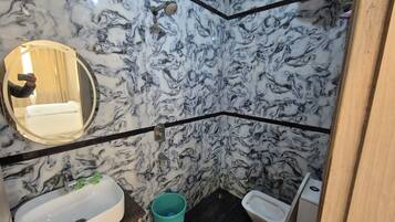Een badkamer met een marmeren wand, een wastafel, een spiegel, een bidet en een emmer.
