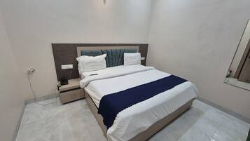 Een net opgemaakt bed met een blauwe deken, een nachtkastje met een telefoon en een stopcontact.