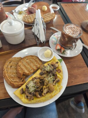 Un desayuno con tostadas, una tortilla y una bebida caliente sobre una mesa.