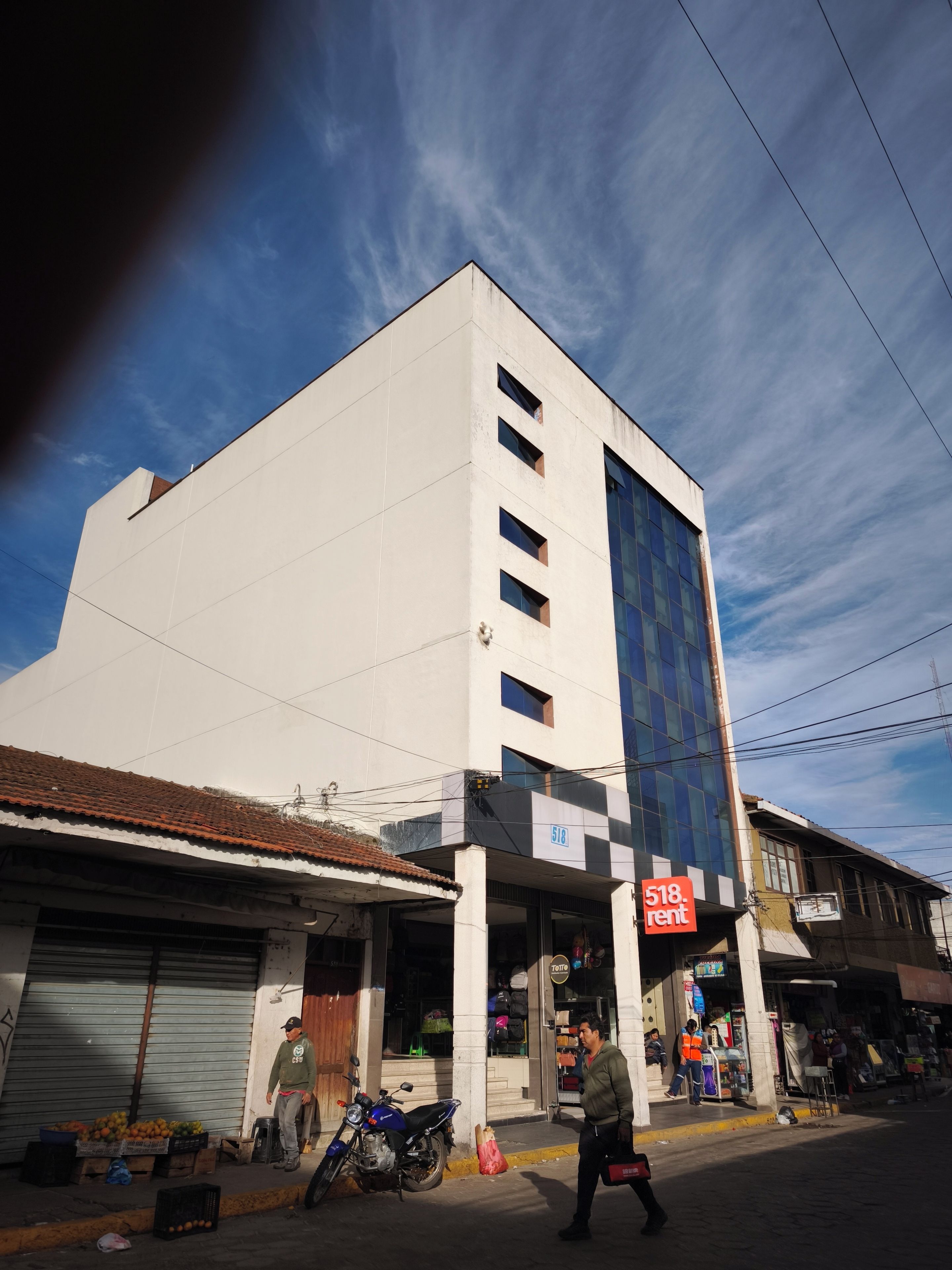 A multi-story building with a ground-level commercial space, a visible sign for a rental service, and a parked motorcycle.