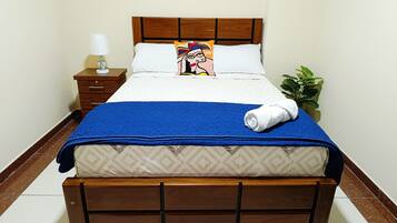 A neatly made bed with a blue blanket, a pillow with a colorful design, and a white towel.