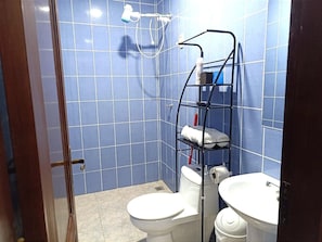 A bathroom with blue tiled walls, a white toilet, a white sink, and a metal shelf with towels.