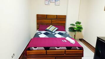 Ein Bett mit hölzernem Kopfteil, einer gemusterten Tagesdecke und einem einzelnen Kopfkissen.