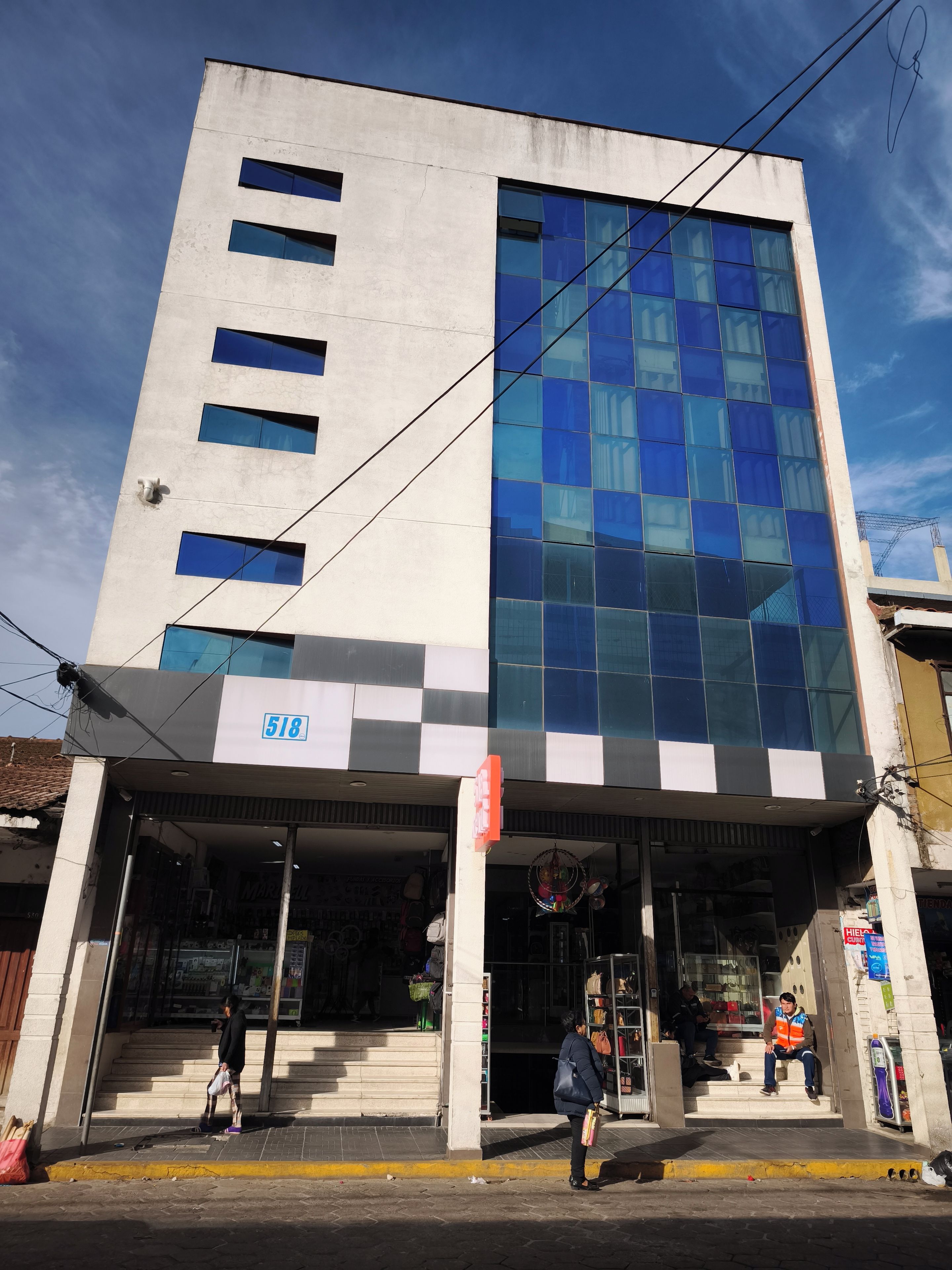 Un edificio de varios pisos con un amplio frente de vidrio, una tienda visible en la planta baja y un cielo despejado al fondo.