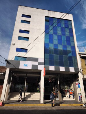 A multi-story building with a large glass facade, a visible storefront at the ground level, and a clear sky in the background.