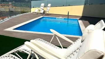 Una piscina en la azotea con sillones de descanso y una vista despejada del paisaje.
