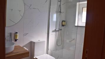 A bathroom with a marble wall, a toilet, a sink with a wooden countertop, and a shower enclosure.