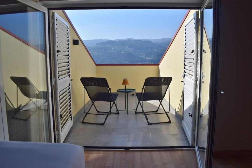 An open balcony with a table and two chairs, a view of the mountains, and a door with a window.