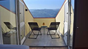 An open balcony with a table and two chairs, a view of the mountains, and a door with a window.