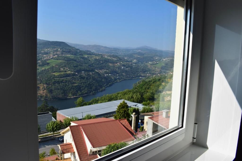 Une vue sur une vallée, avec une rivière, des bâtiments et des collines, depuis une fenêtre.