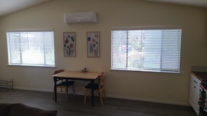 A dining area with a table and chairs, two windows with blinds, and an air conditioning unit on the wall. - Tremendous 1-bedroom house with AC in charming Grants Pass (Grants Pass)