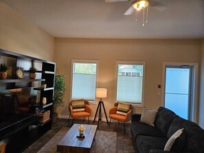 A living room with a sofa, two armchairs, a coffee table, a TV, and a lamp.
